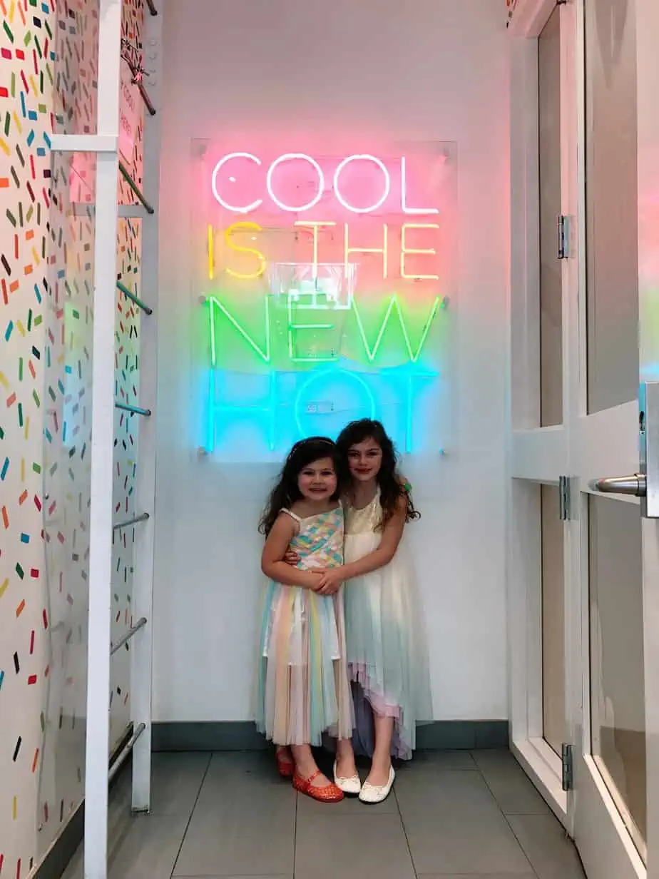 Kids standing in front of the Cool Mess restaurant's neon sign 