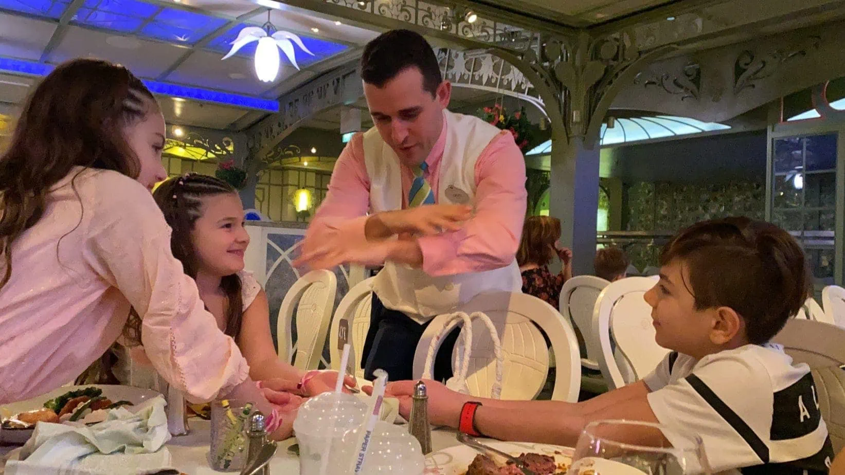 Waiter in white vest and pink shirt entertaining kids at a Disney Cruise restaurant 