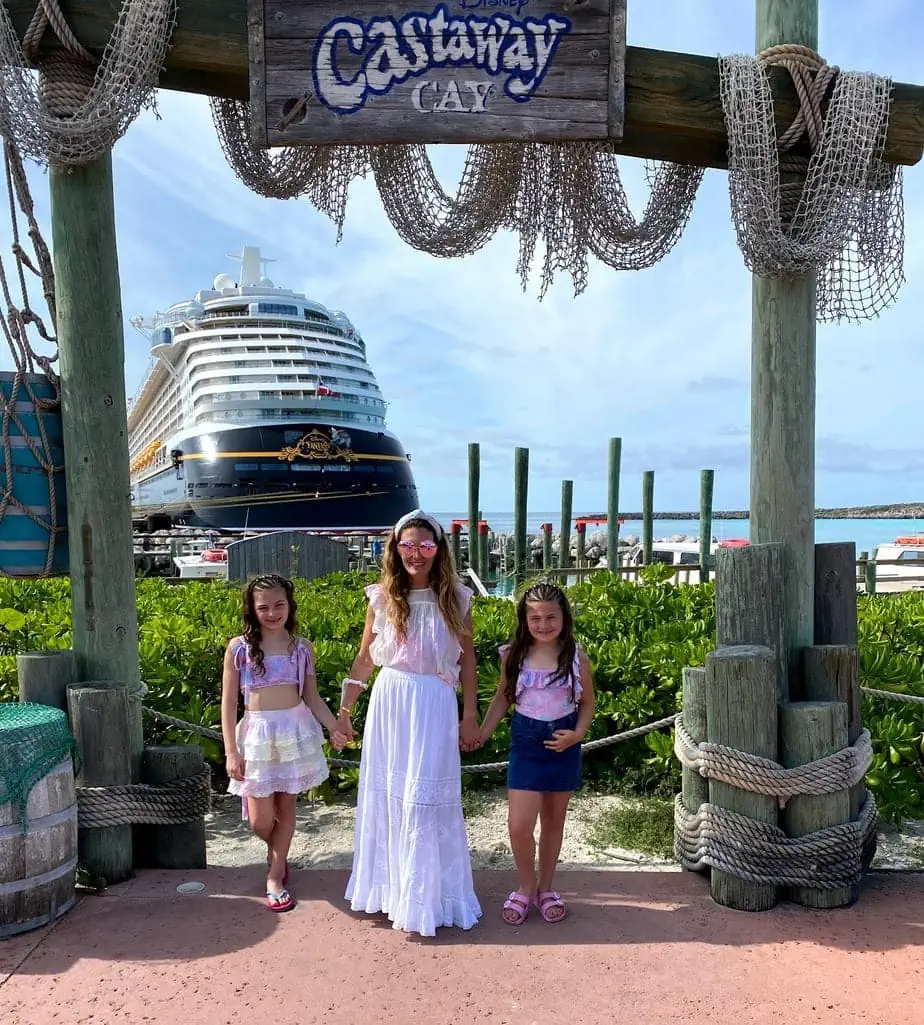 Mother and daughters in pink, girly outfits standing underneath Castaway sign with Disney Cruise in background