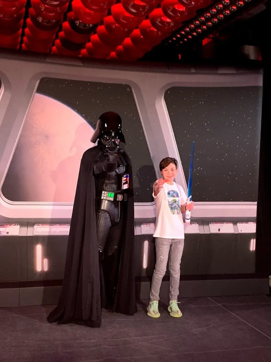 Son posing with Darth Vader character while holding blue lightsaber 