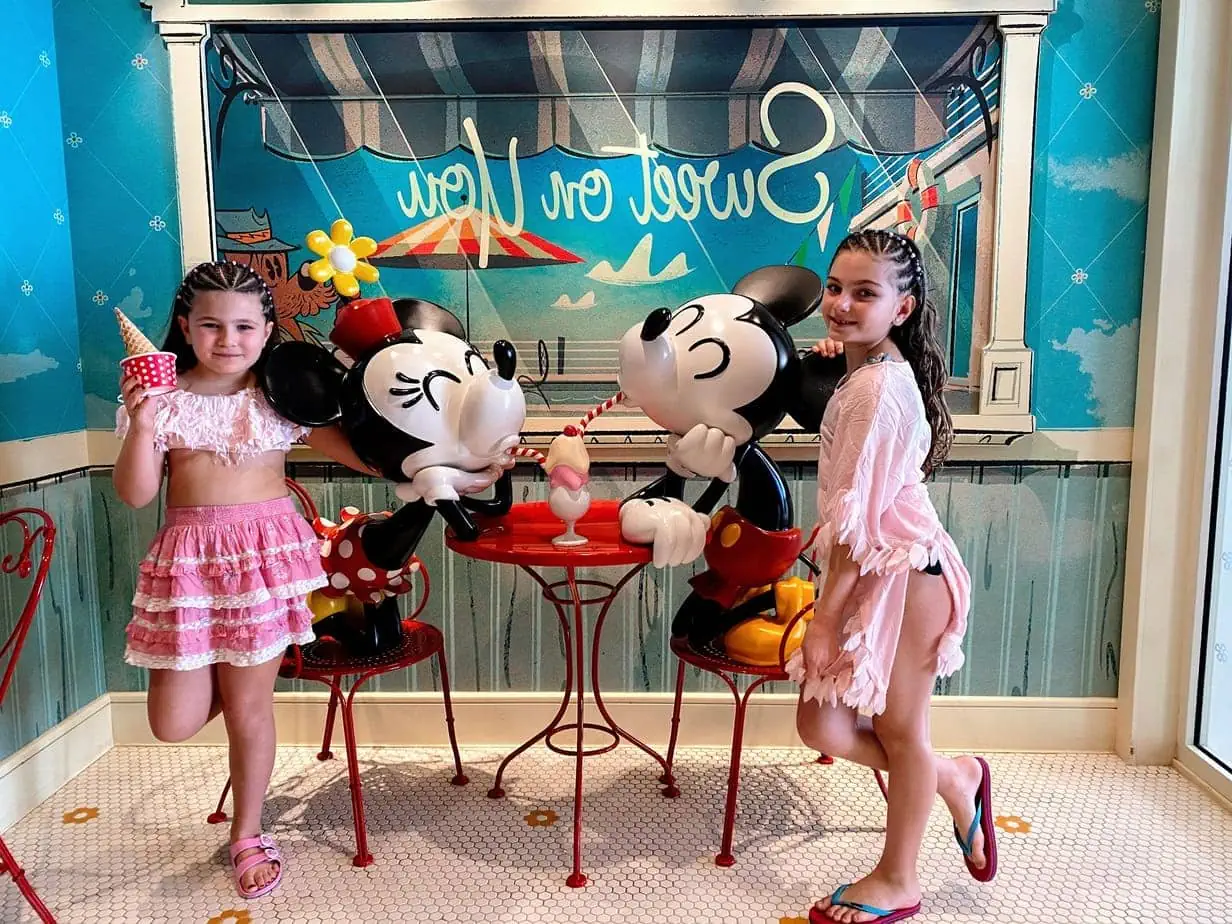 Daughters in all-pink outfits posing with ice cream snacks and Mickey and Minnie Mouse figurines on Disney Cruise
