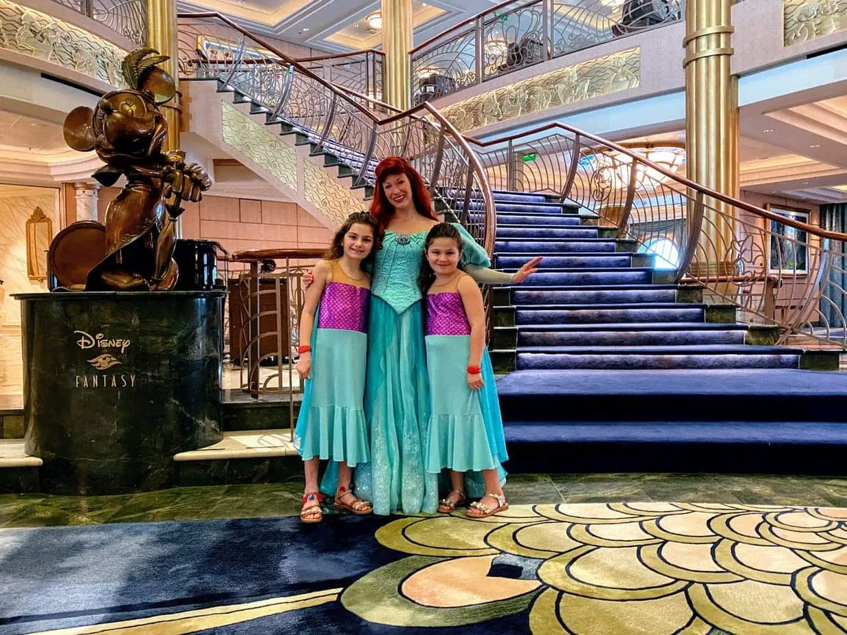Daughters wearing matching mermaid outfits posing with Ariel character from the movie "The Little Mermaid" 