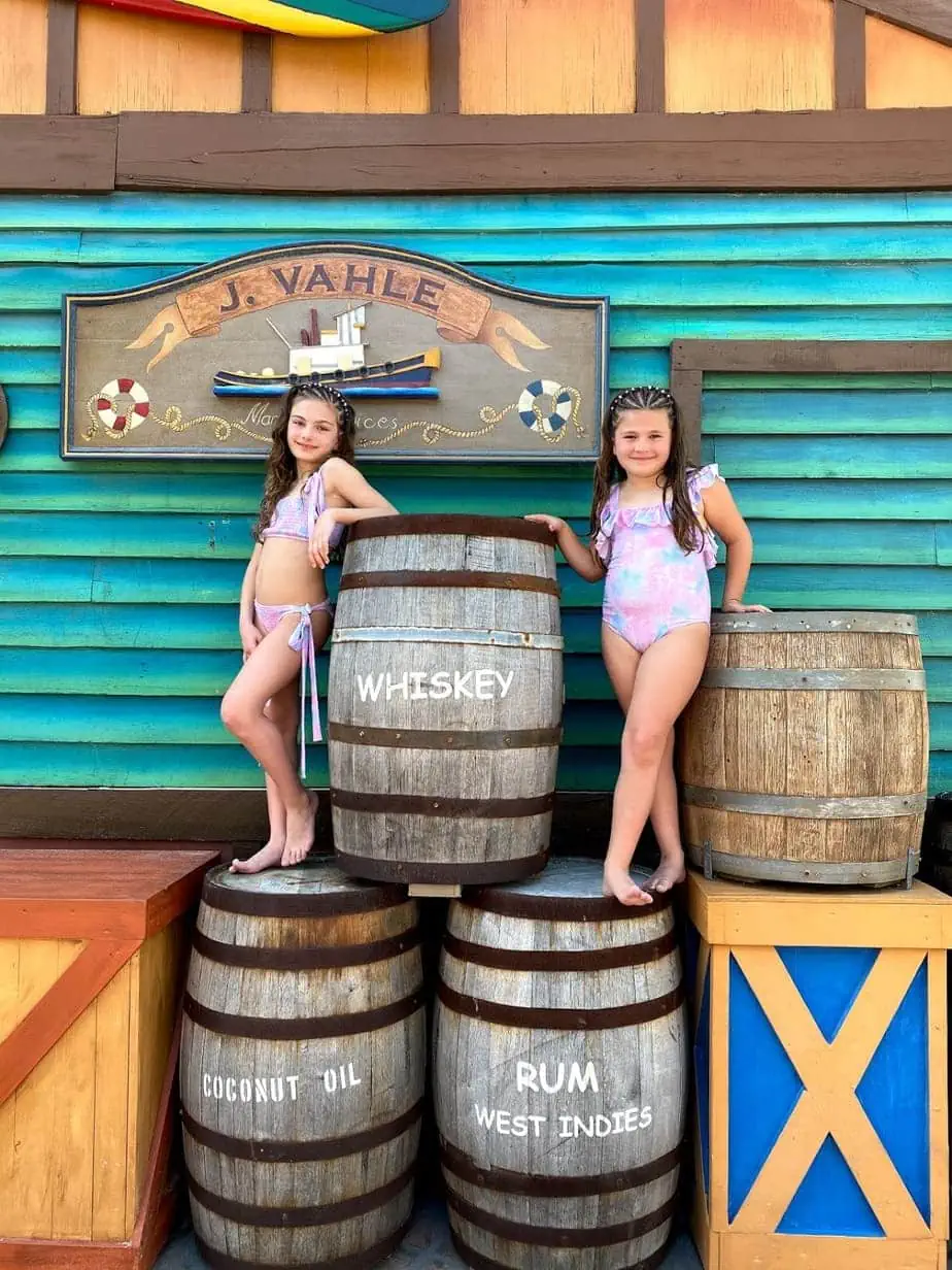 Daughters in swimsuits wearing pastel swimsuits standing ontop of fake rum and whiskey ship barrels