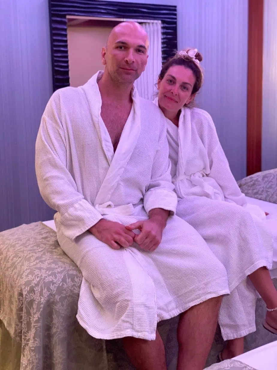 Couple wearing matching white spa robes while sitting on massage chair