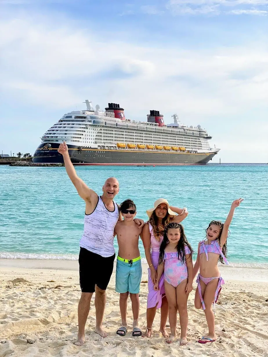 Family excited on beach with Disney Cruise ship floating on blue ocean in background