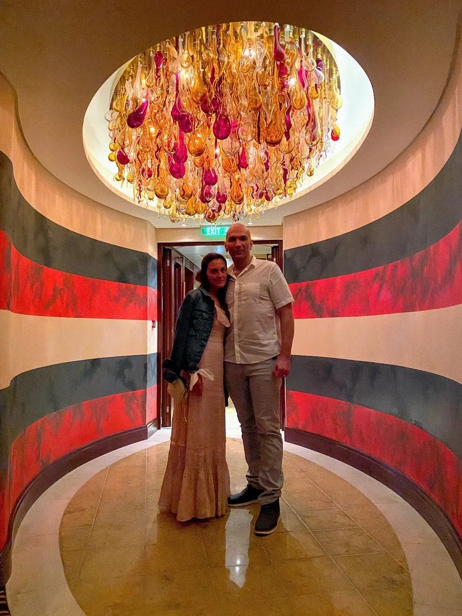 Brianne and Jason smiling in entry way to a Disney cruise restaurant underneath a red and orange bottle chandelier 