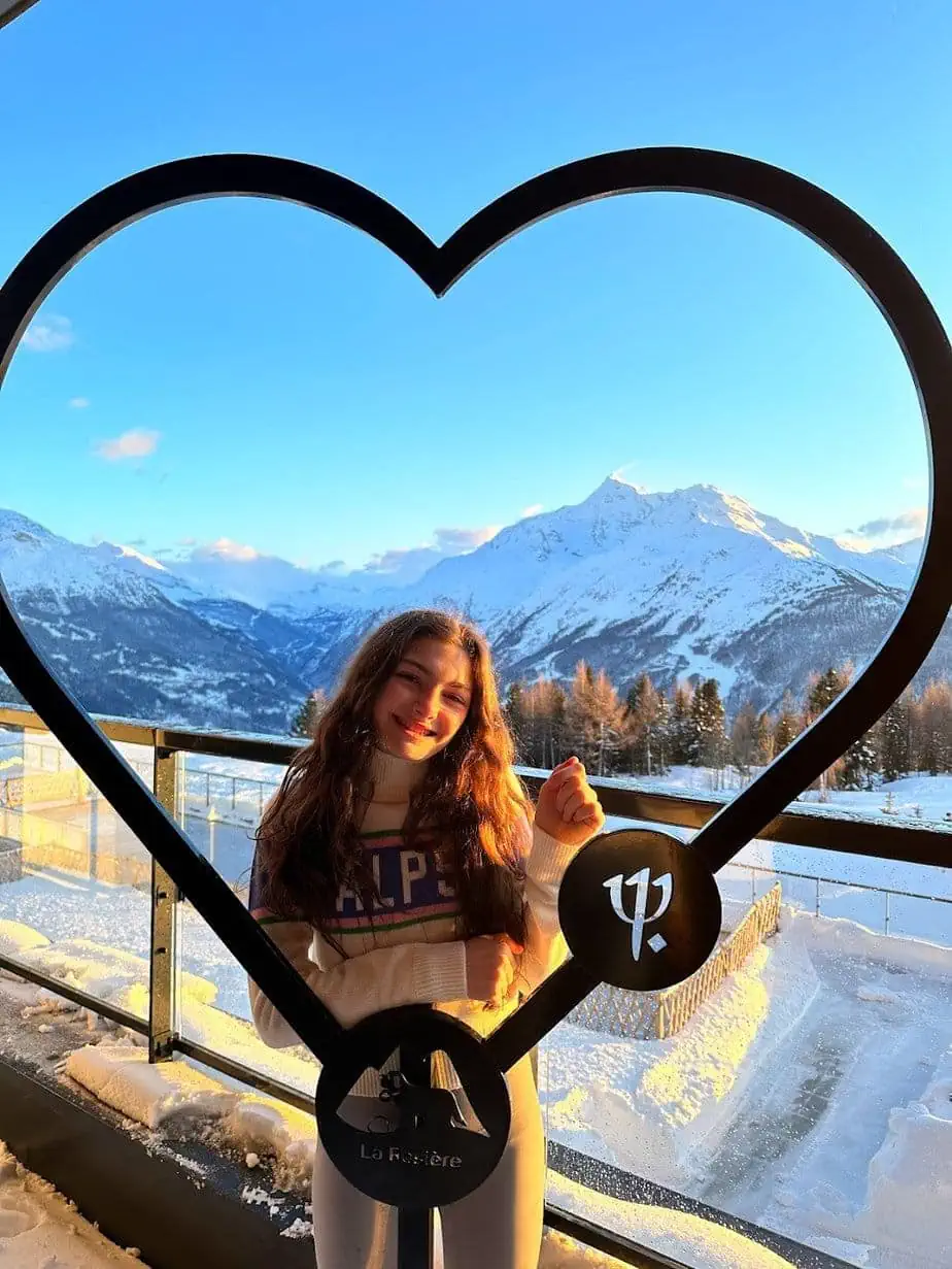 Daughter posing in heart symbol at ski resort with mountains in background.