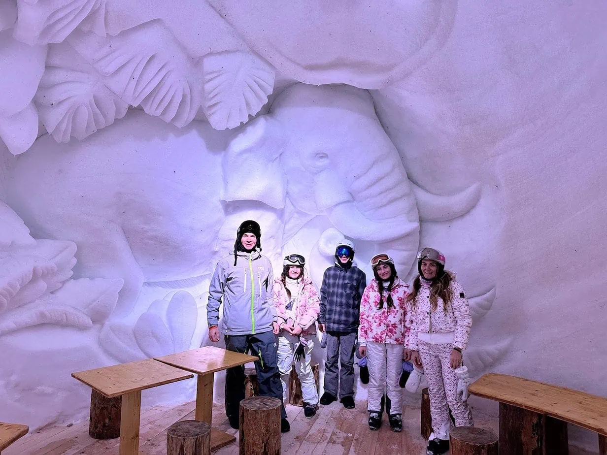 Family in ski gear posing in front of ice sculptures in a igloo ski lounge