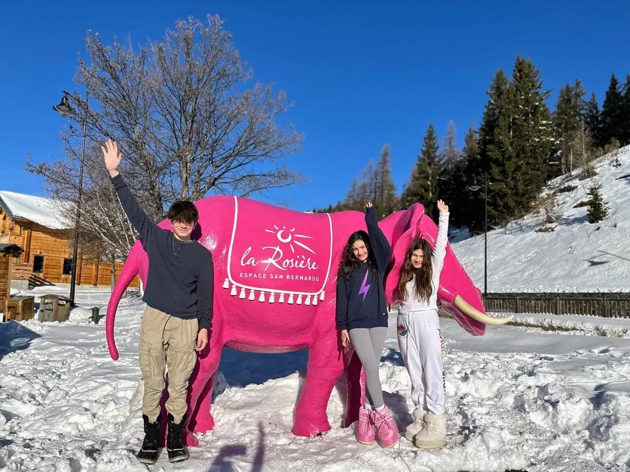 Kids posing with pink "La Rosiere" cow statue on snowy ski mountain