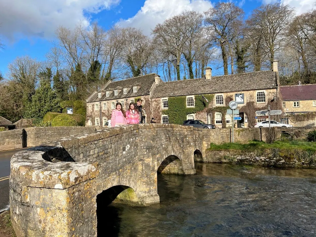 Kids posing on bridge leading to magical, stone hotel in Cotswolds, England