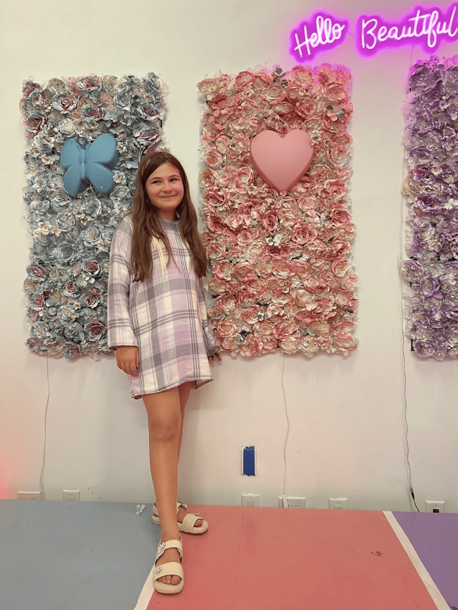 Daughter in trendy fall pink plaid dress in front of cute floral decor