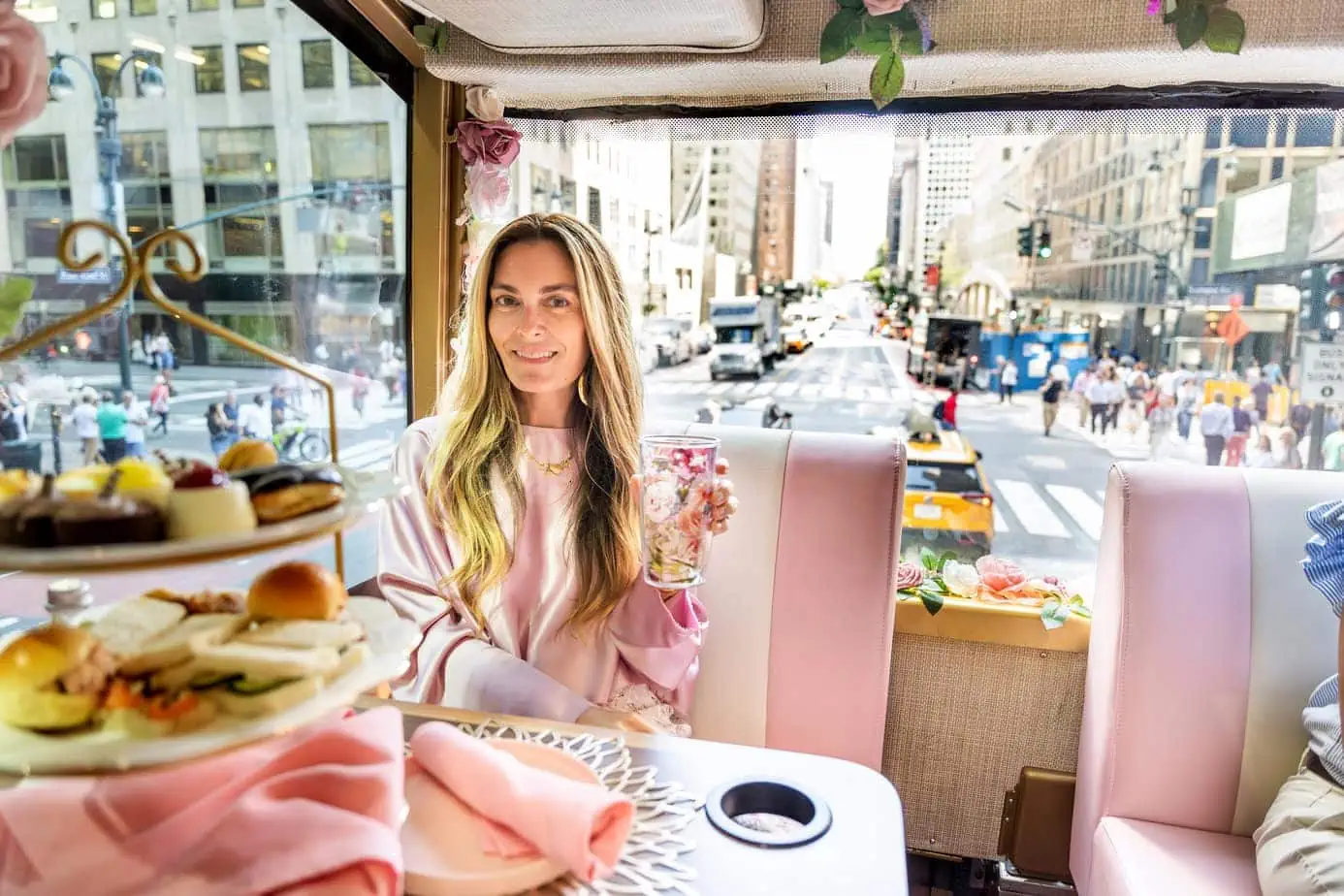 Brianne sitting in pink decorated Tea Around Town with high tea desserts and sandwiches on table