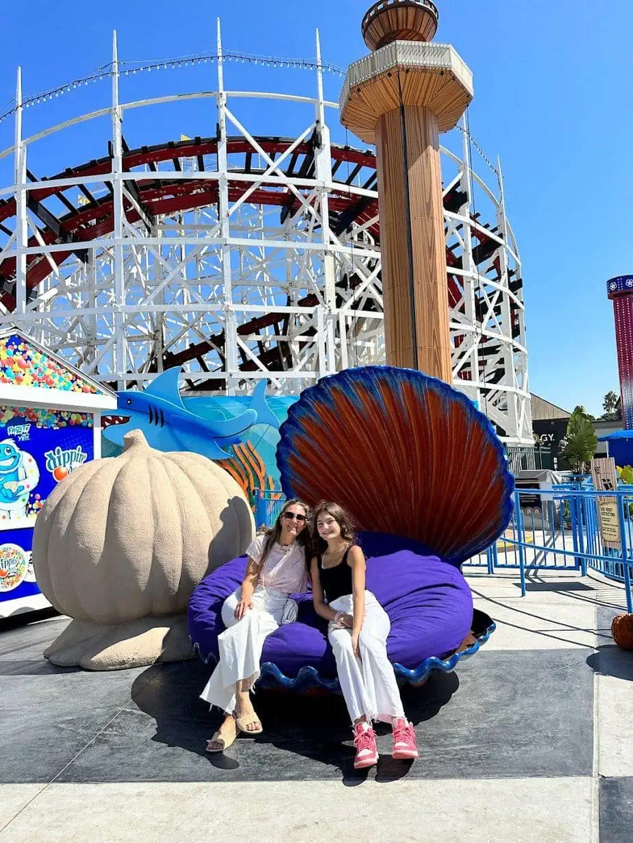 Mother and Daughter posing in sea-shell photo opportunity at Belmont Park amusement park with rollercoaster in background
