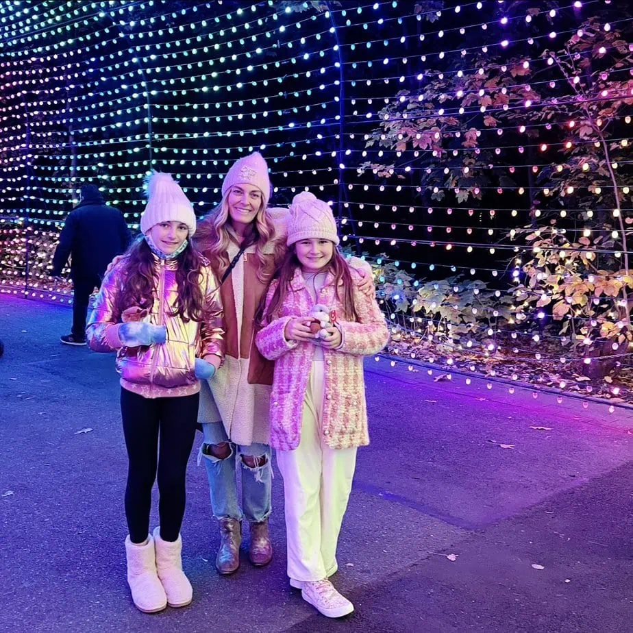Brianne and her daughters in cute winter hats standing in bright lights of the Bronx Zoo Holiday Lights NYC activity